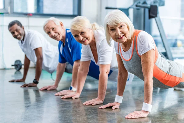 Deportistas multiculturales senior feliz haciendo tablón en el gimnasio — Stock Photo