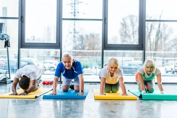 Athlètes seniors faisant de l'exercice sur tapis de fitness au gymnase — Photo de stock