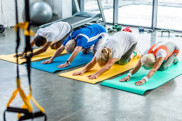 Visão de alto ângulo de atletas seniores exercício síncrono em tapetes de fitness no ginásio — Fotografia de Stock