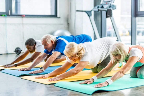 Atletas mayores alegres ejercicio síncrono en alfombras de fitness en el gimnasio - foto de stock