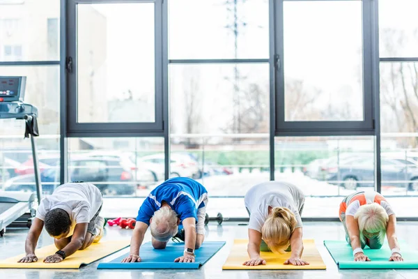 Senior sportivi esercizio sincrono su tappetini fitness in palestra — Foto stock