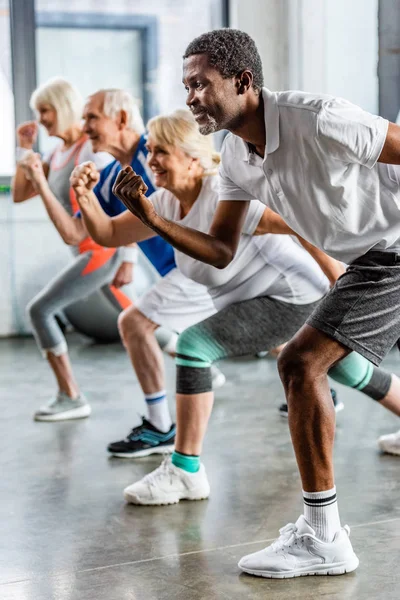 African american sportsman synchronous exercising with friends at sports hall — Stock Photo