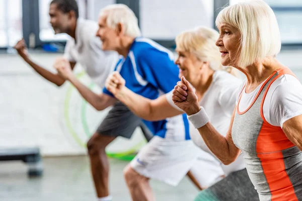 Selective focus of senior sportswoman exercising with friends at gym — Stock Photo