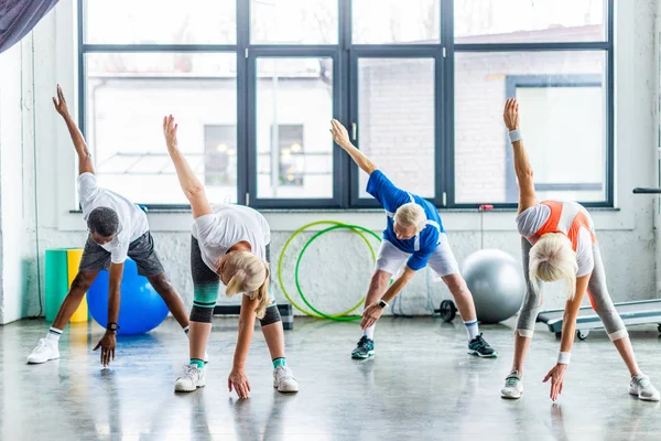 Multicultural senior sportspeople synchronous exercising at sports hall — Stock Photo