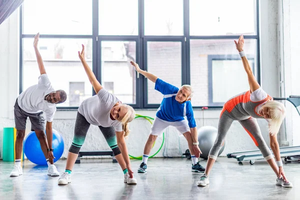 Sportivi anziani multietnici esercizio sincrono presso palazzetto dello sport — Foto stock