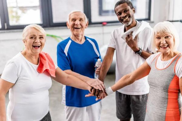 Сміючись старші мультикультурні спортсмени складають руки в спортивному залі — стокове фото