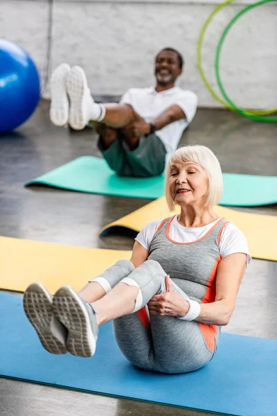 Foco seletivo da mulher idosa e seu marido se exercitando em tapetes de fitness no ginásio — Fotografia de Stock