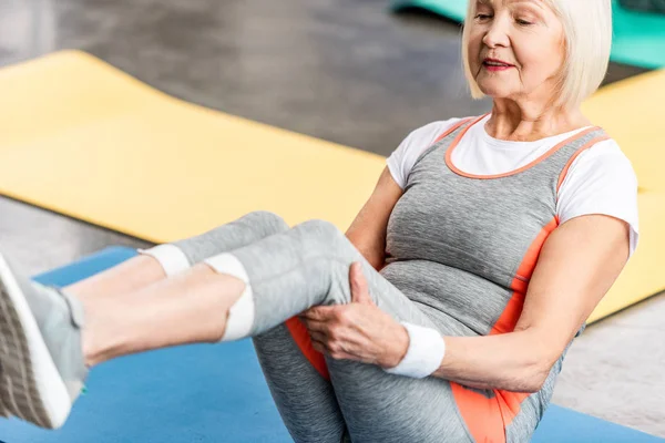 Selective focus of senior sportswoman exercising on fitness mat at gym — Stock Photo