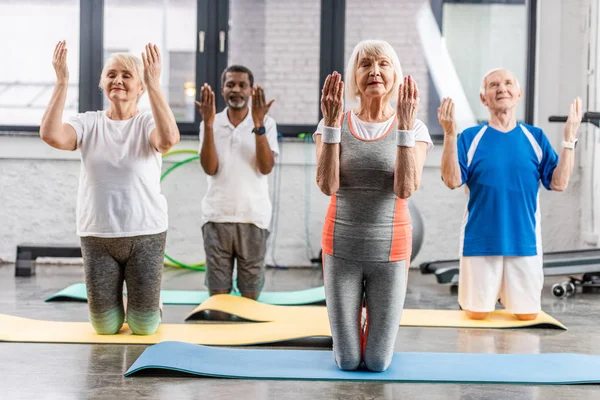 Atletas senior multiétnicos ejercicio síncrono en colchonetas de fitness en el gimnasio - foto de stock