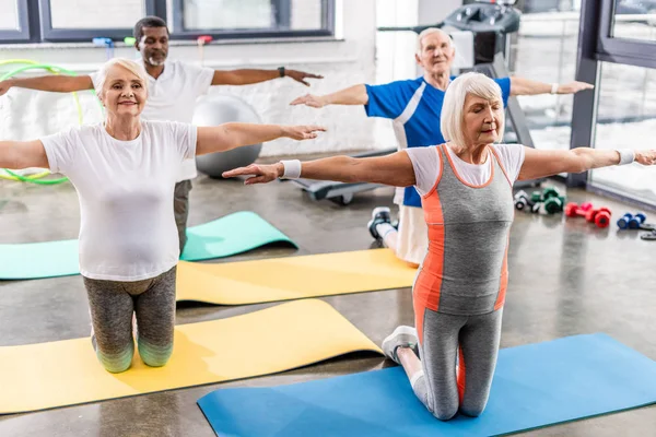 Foco seletivo de atletas multiculturais seniores exercício síncrono em tapetes de fitness no ginásio — Fotografia de Stock