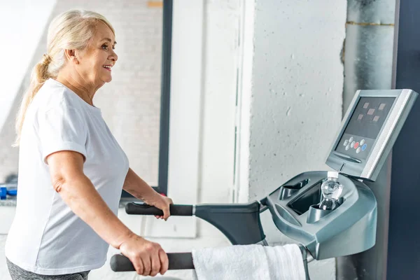 Side view of smiling senior sportswoman running on treadmill at sports hall — Stock Photo