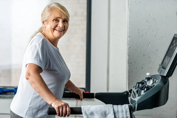 Happy senior sportswoman running on treadmill at sports hall — Stock Photo