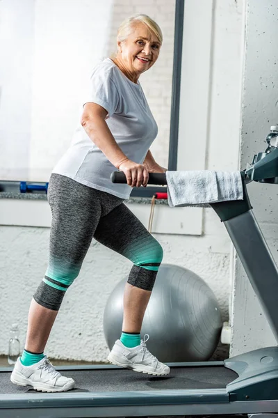 Smiling senior sportswoman running on treadmill at sports hall — Stock Photo