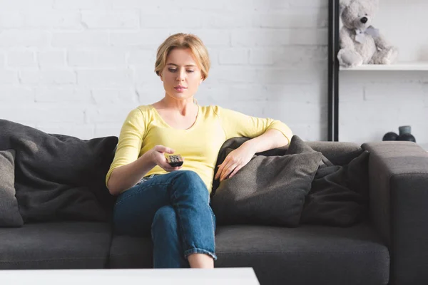 Attraktive Frau sitzt auf der Couch und bedient Fernbedienung — Stockfoto