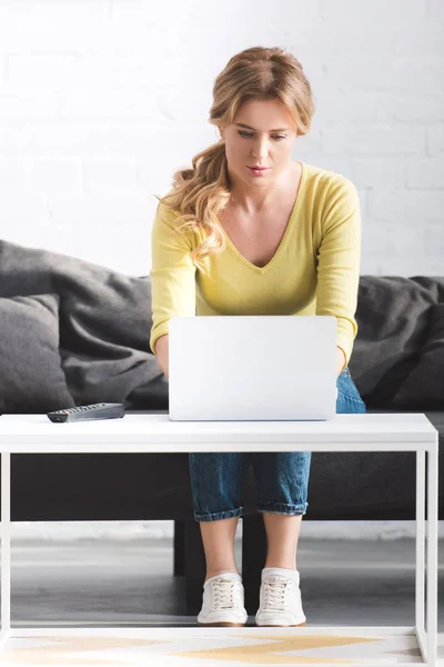 Attraktive fokussierte Frau, die auf der Couch sitzt und zu Hause Laptop benutzt — Stockfoto