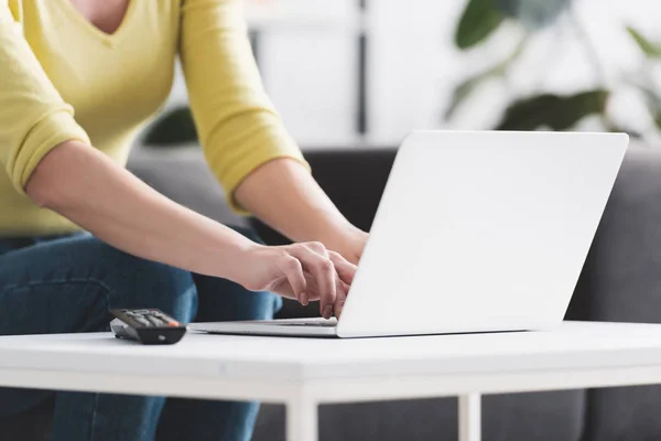 Tiro cortado de mulher sentada no sofá e usando laptop — Fotografia de Stock