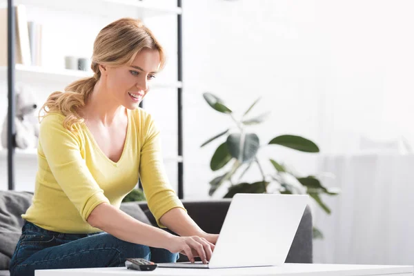 Bela mulher sorridente sentado no sofá e usando laptop — Fotografia de Stock