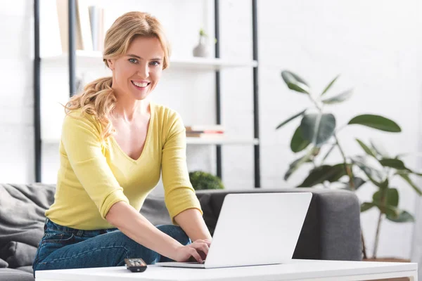 Atractiva mujer usando el ordenador portátil y sonriendo a la cámara en casa - foto de stock