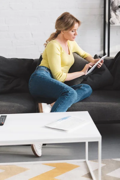 Bela mulher sentada no sofá e usando tablet digital em casa — Fotografia de Stock