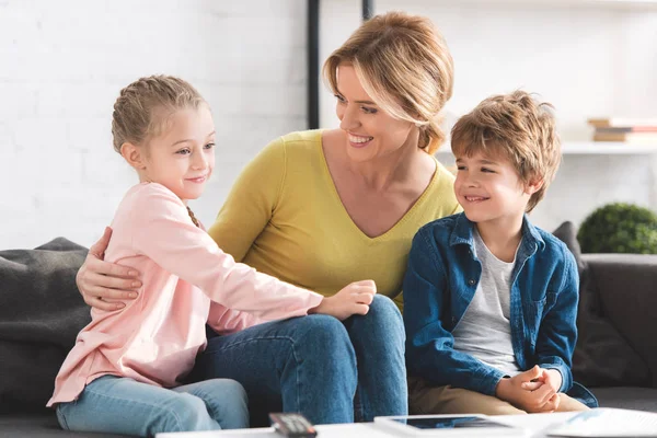Happy mother looking at adorable smiling children sitting together on couch — Stock Photo