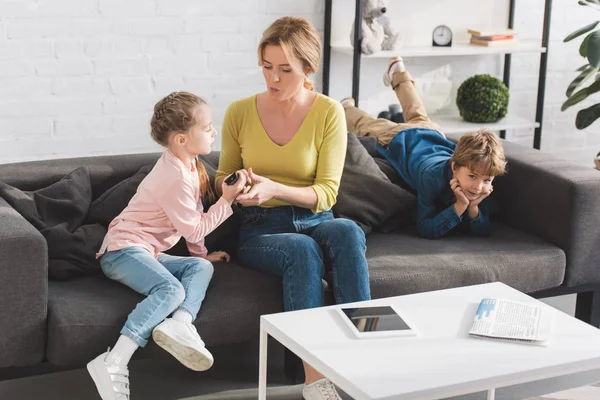 Madre e hija sosteniendo mando a distancia mientras niño acostado en el sofá en casa - foto de stock