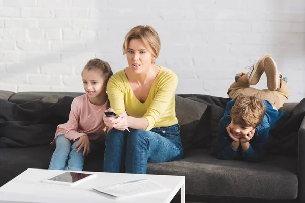 Мати з чарівними дітьми сидить на дивані і дивиться телевізор разом — стокове фото