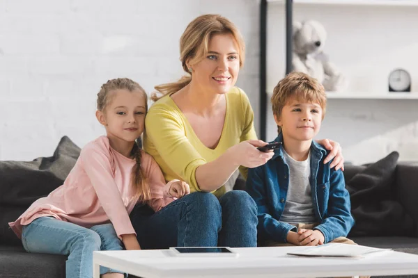 Madre feliz usando el mando a distancia y viendo la televisión juntos en casa - foto de stock