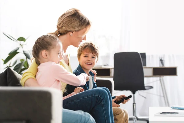 Happy mother with adorable kids watching tv together at home — Stock Photo