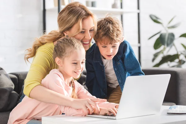 Glückliche Mutter mit entzückend lächelnden Kindern, die zu Hause gemeinsam Laptop benutzen — Stockfoto