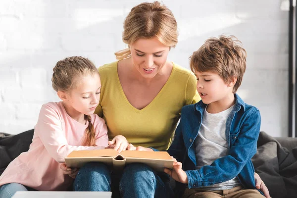 Happy mother with adorable children reading book together at home — Stock Photo