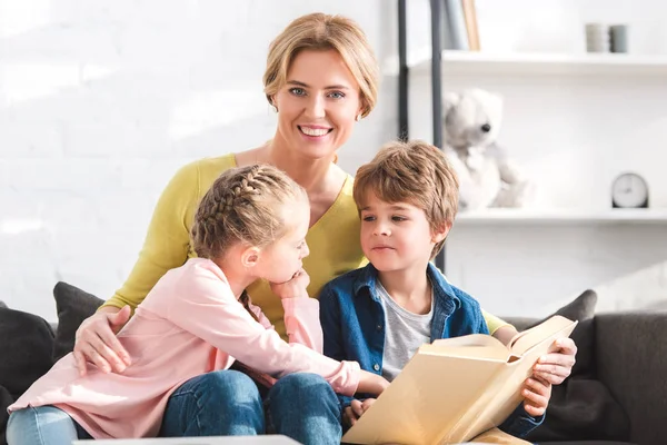 Mère heureuse souriant à la caméra tout en lisant le livre avec les enfants — Photo de stock