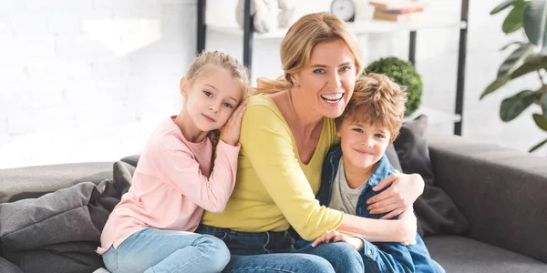 Glückliche Mutter mit entzückenden Kindern, die sich umarmen und in die Kamera lächeln — Stockfoto