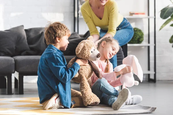 Schnappschuss einer glücklichen Mutter, die auf der Couch sitzt und niedlichen kleinen Kindern, die zu Hause mit Spielzeug spielen — Stockfoto