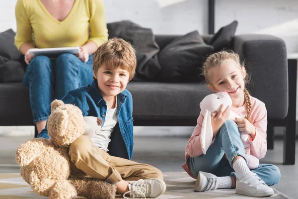 Cropped shot of mother sitting on couch while smiling kids playing wityh toys at home — Stock Photo