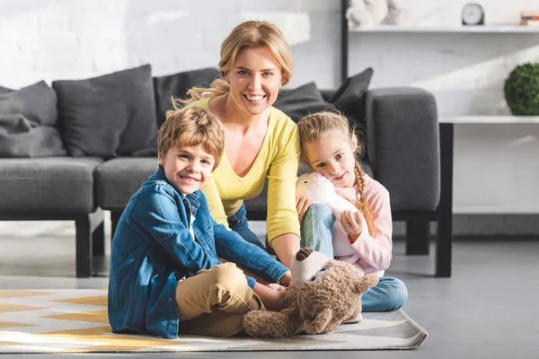 Glückliche Mutter mit niedlichen kleinen Kindern, die zusammen spielen und in die Kamera lächeln — Stockfoto