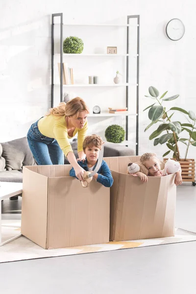 Emotional mother looking at naughty children playing in cardboard boxes — Stock Photo