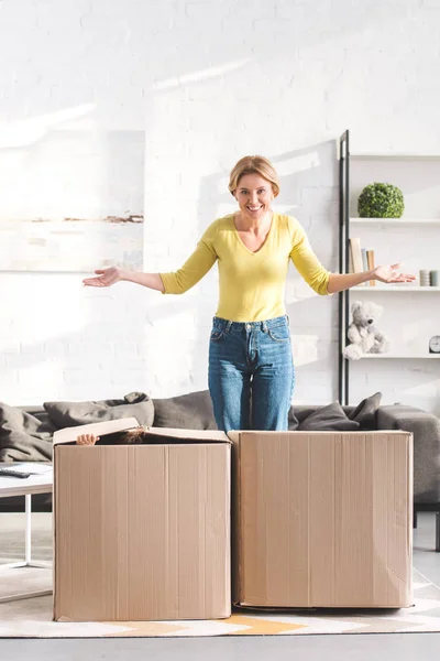 Happy mother smiling at camera while playing with children hiding in cardboard boxes — Stock Photo