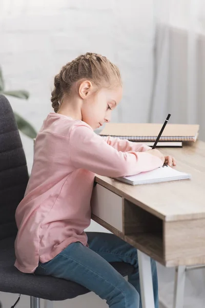 Hermoso niño enfocado sentado en el escritorio y estudiando en casa - foto de stock