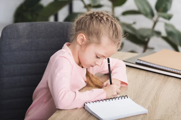 Adorable niño sentado en el escritorio y estudiando en casa - foto de stock