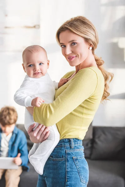 Hermosa feliz madre sosteniendo adorable bebé niño y sonriendo a la cámara - foto de stock
