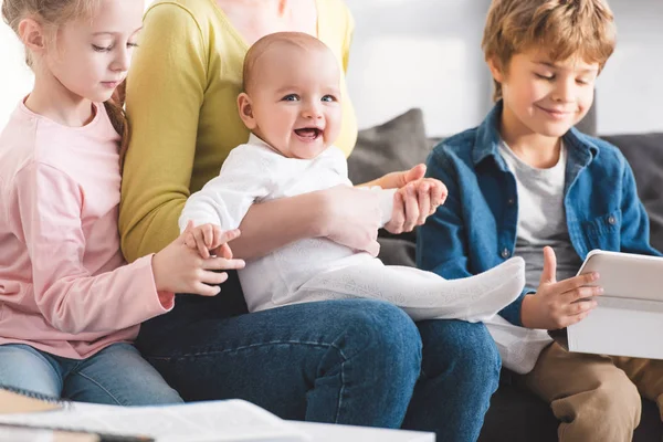 Cropped shot of mother with infant child and cute siblings sitting together in sofa — Stock Photo