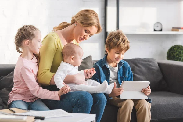 Beautiful happy mother with three adorable children sitting together on sofa — Stock Photo