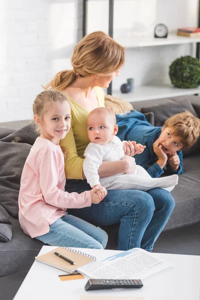 Schöne Mutter mit entzückend glücklichen Kindern, die zusammen auf dem Sofa sitzen — Stockfoto