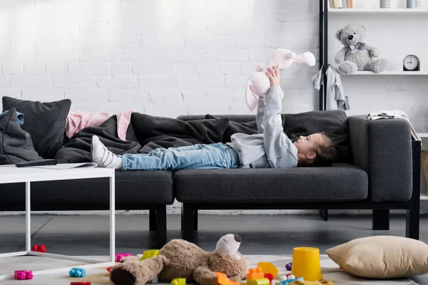 Toys on carpet and beautiful child playing on sofa behind — Stock Photo