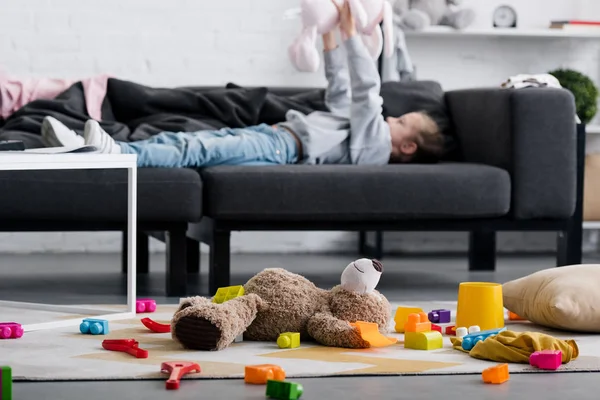 Іграшки на килимі і дитина лежить на дивані позаду — стокове фото