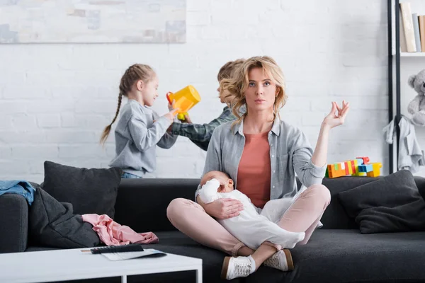 Mãe com criança infantil meditando na posição de lótus e olhando para a câmera enquanto irmãos impertinentes brincando atrás — Fotografia de Stock