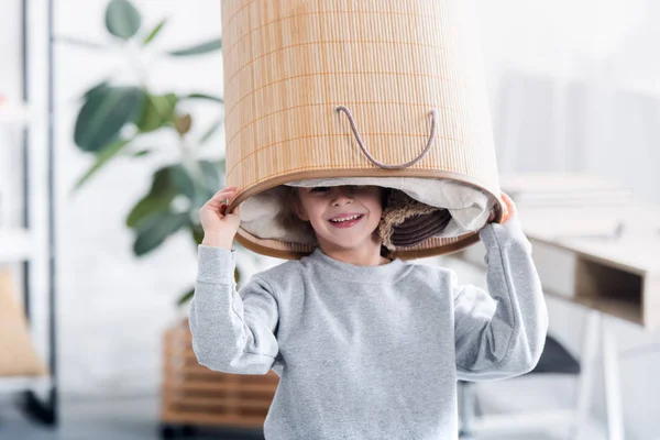 Criança feliz bonito brincando com cesta de lavanderia na cabeça — Fotografia de Stock