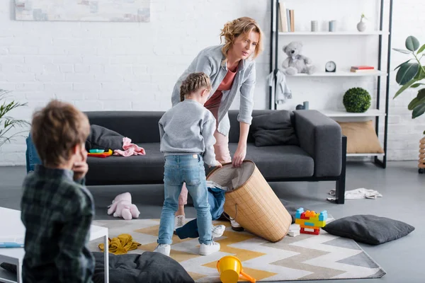 Müde Mutter legt Spielzeug in Korb, während freche Kinder zu Hause spielen — Stockfoto