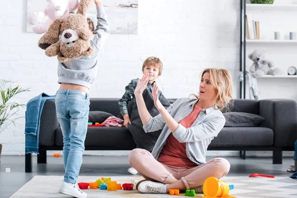 Asustada madre cansada mirando a los niños traviesos jugando en casa - foto de stock