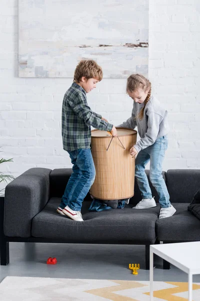 Crianças safadas segurando cesta no sofá em casa — Fotografia de Stock